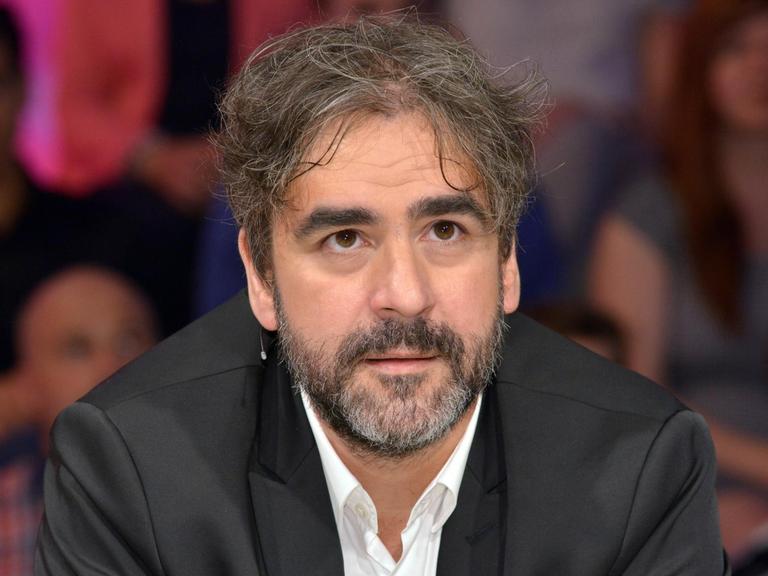 Yücel sitzt als Gast einer Talkshow auf dem Podium.