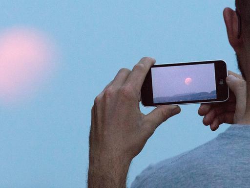 Ein Mann fotografiert den Mond mit seinem Smartphone.