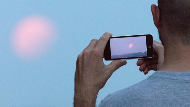 Ein Mann fotografiert den Mond mit seinem Smartphone.