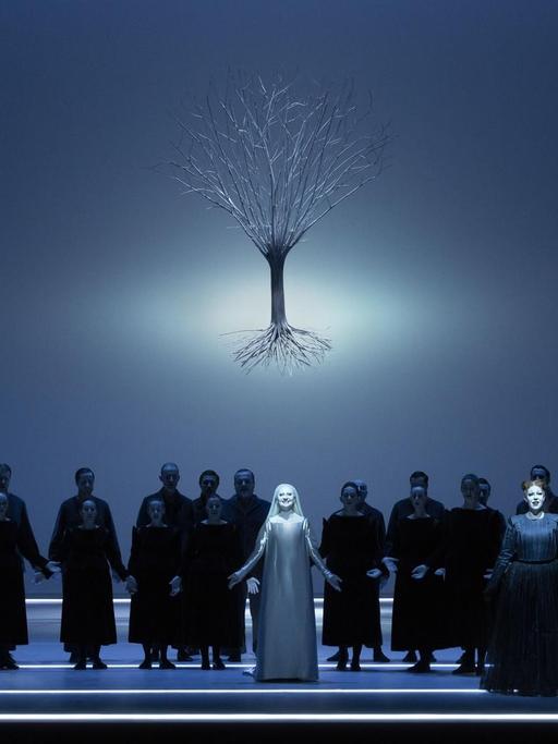 Bläulich schimmernde Szene aus dem Oratorium "Der Messias" in der Inszenierung von Robert Wilson bei der Mozartwoche 2020 in Salzburg: Chor und Solisten stehen auf der Bühne, über ihnen schwebt das Bild eines Baumes mit Wurzelwerk.
