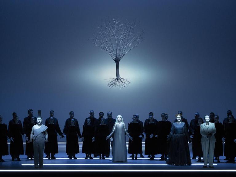 Bläulich schimmernde Szene aus dem Oratorium "Der Messias" in der Inszenierung von Robert Wilson bei der Mozartwoche 2020 in Salzburg: Chor und Solisten stehen auf der Bühne, über ihnen schwebt das Bild eines Baumes mit Wurzelwerk.