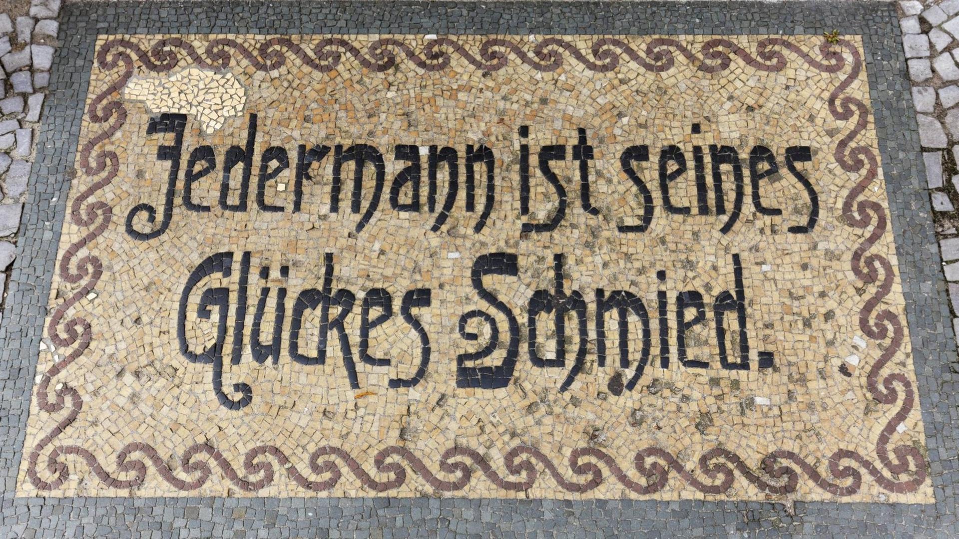 Ein Bodenmosaik in Neuruppin mit dem Sinnspruch "Jedermann ist seines Glückes Schmied" Ein Bodenmosaik in Neuruppin mit dem Sinnspruch "Jedermann ist seines Glückes Schmied"