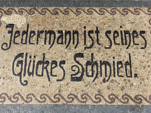 Ein Bodenmosaik in Neuruppin mit dem Sinnspruch "Jedermann ist seines Glückes Schmied"