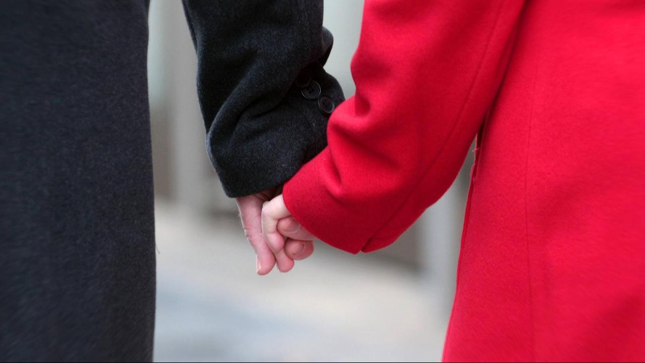 Paar mit roter und schwarzer Jacke halten die Hände bei einem Spaziergang Paar mit roter und schwarzer Jacke halten die Hände bei einem Spaziergang