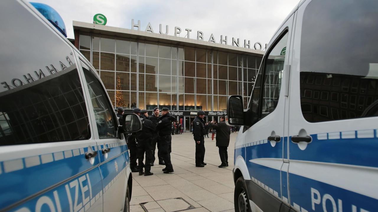 Polizisten zwischen zwei Polizeiautos vor dem Kölner Hauptbahnhof.