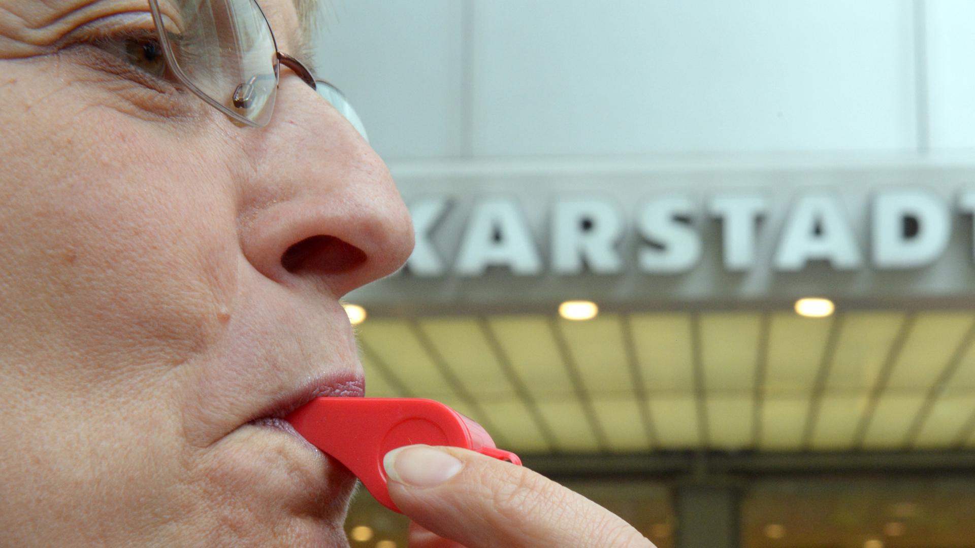 Bei einem Streik bläst eine Karstadt-Beschäftigte vor einem Warenhaus in Berlin in eine Trillerpfeife.