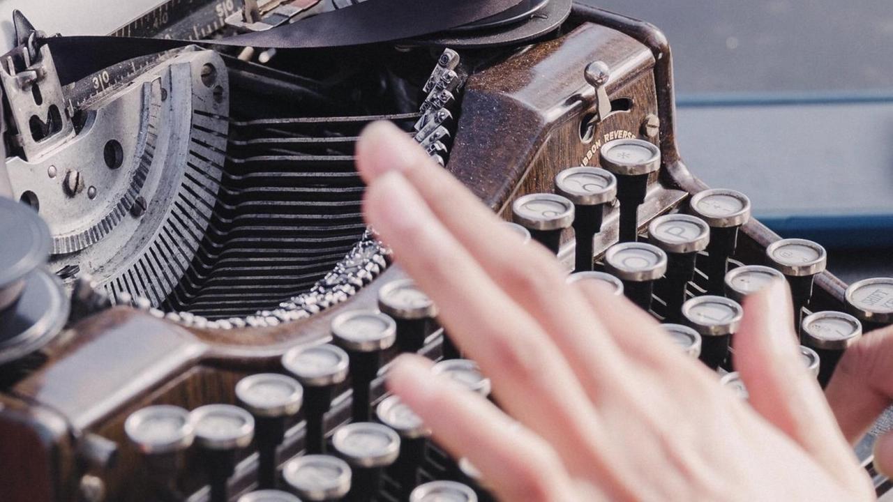 Fotografie einer weiblichen Hand in der Unschärfe vor einer Schreibmaschine. Fotografie einer weiblichen Hand in der Unschärfe vor einer Schreibmaschine.