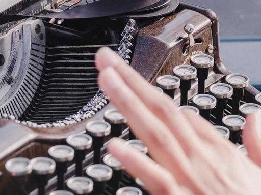 Fotografie einer weiblichen Hand in der Unschärfe vor einer Schreibmaschine.