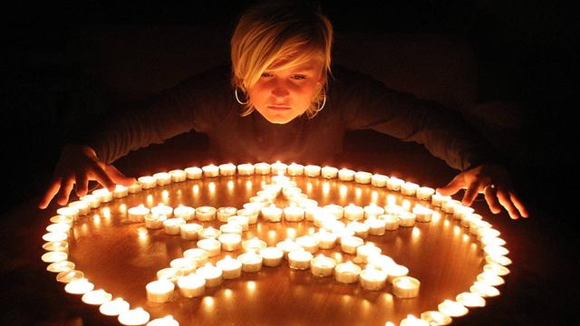 Eine junge Frau beugt sich über Kerzen, die in der Form eines Pentagramms innerhalb eines Kreises aufgestellt sind.