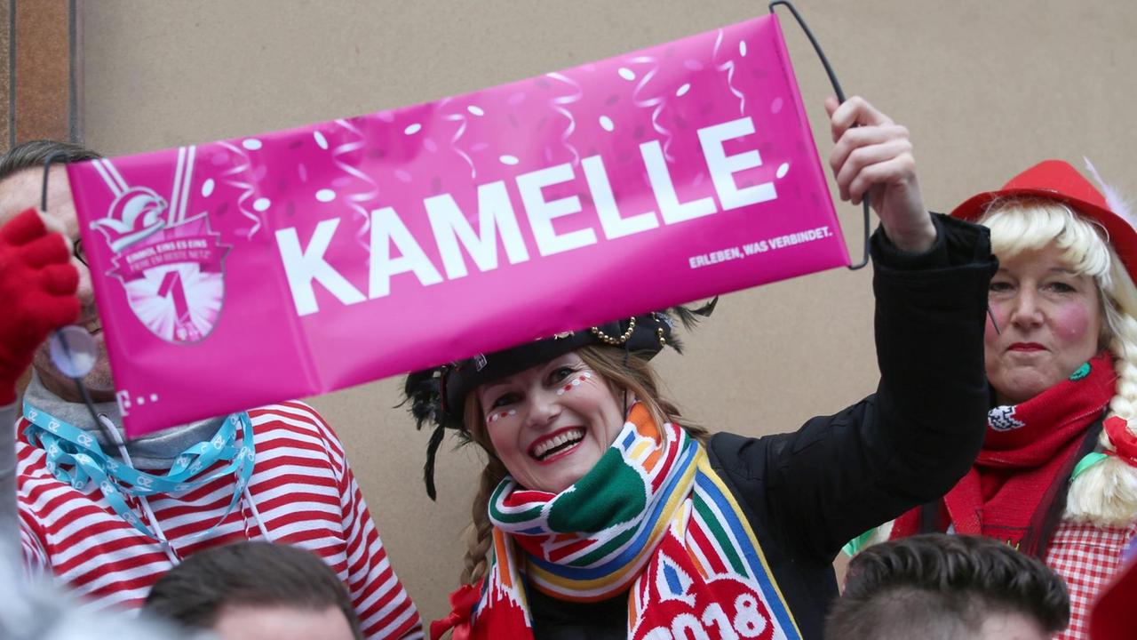 12.02.2018, Nordrhein-Westfalen, Köln: Kostümierte Karnevalisten nehmen am Rosenmontagszug teil. Sie halten ein Banner mit der Aufschrift "Kamelle" hoch