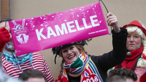 12.02.2018, Nordrhein-Westfalen, Köln: Kostümierte Karnevalisten nehmen am Rosenmontagszug teil. Sie halten ein Banner mit der Aufschrift "Kamelle" hoch