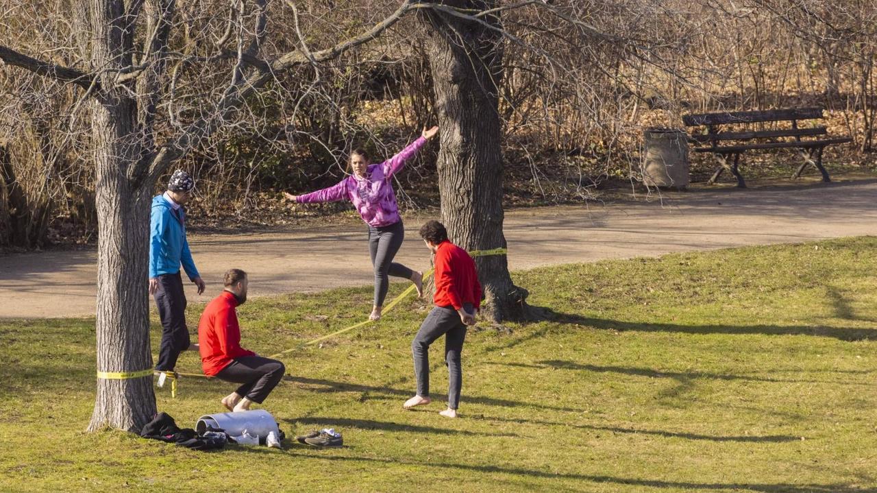 Junge Leute trainieren auf einer Slackline, die zwischen zwei Bäumen gespannt ist.