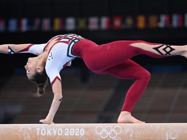 Eine Frau turnt bei den Olympischen Spielen auf einem Schwebebalken, Frauen, sie trägt einen bordeauxrot-weißen Ganzkörperanzug. Es handelt sich um die deutsche Turnerin Pauline Schäfer.