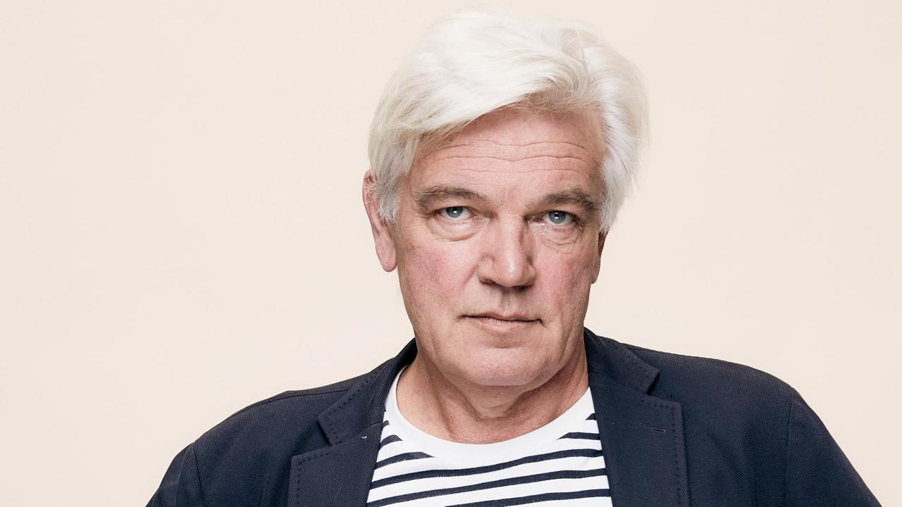 Heino Deckert, ein Mann mit weißen Haaren, schaut in die Kamera. Er trägt eine dunkle Jacke und ein geringeltes Shirt. Heino Deckert, ein Mann mit weißen Haaren, schaut in die Kamera. Er trägt eine dunkle Jacke und ein geringeltes Shirt.