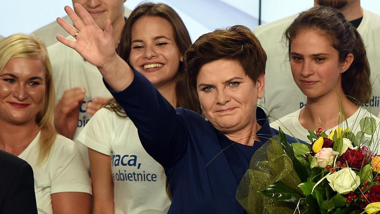 Szydlo steht mit einem Blumenstrauss vor weißgekleideten Unterstützern und winkt. Szydlo steht mit einem Blumenstrauss vor weißgekleideten Unterstützern und winkt.