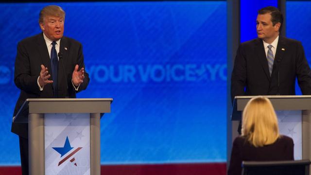 Donald Trump gestikuliert an einem Rednerpult, rechts von ihm hört Ted Cruz zu.