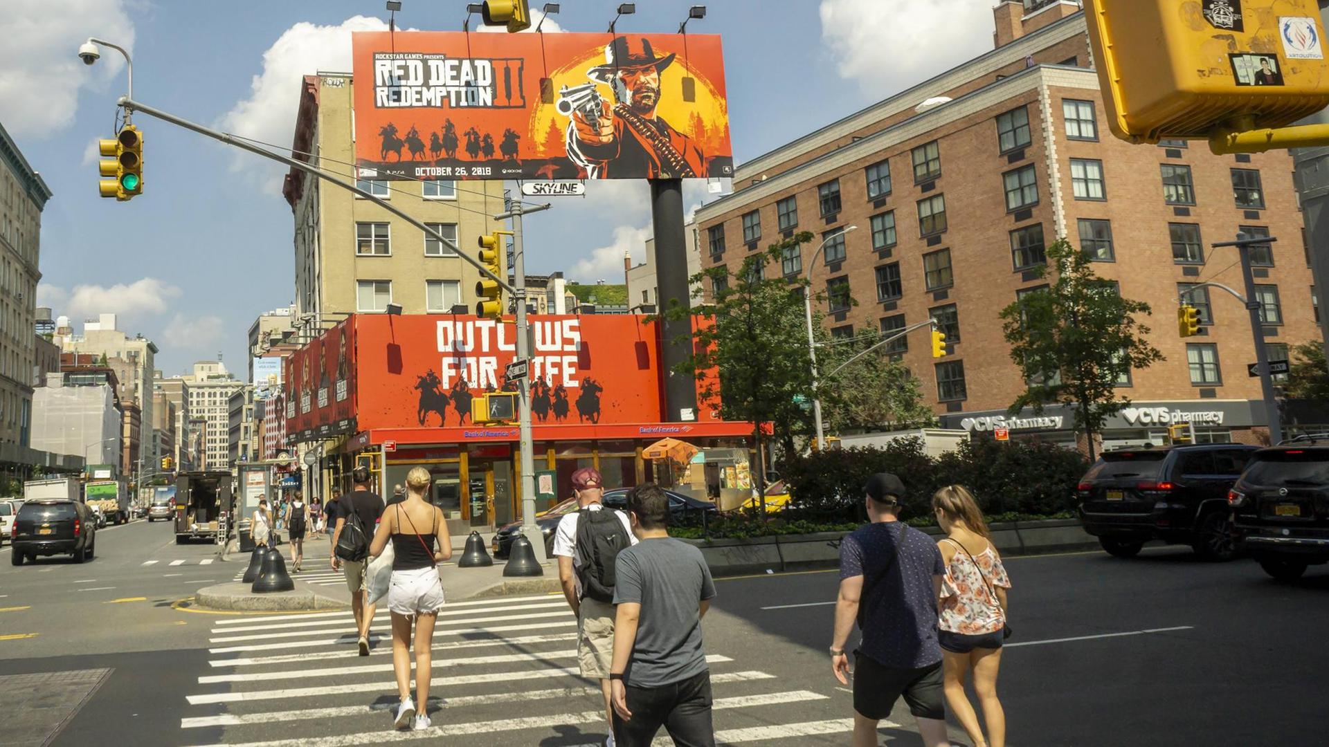 Passanten laufen über einen Zebrastreifen, vor ihnen sind zwei große Plakate zu sehen, auf denen das Computerspiel "Red Dead Redemption 2" beworben wird Passanten laufen über einen Zebrastreifen, vor ihnen sind zwei große Plakate zu sehen, auf denen das Computerspiel "Red Dead Redemption 2" beworben wird