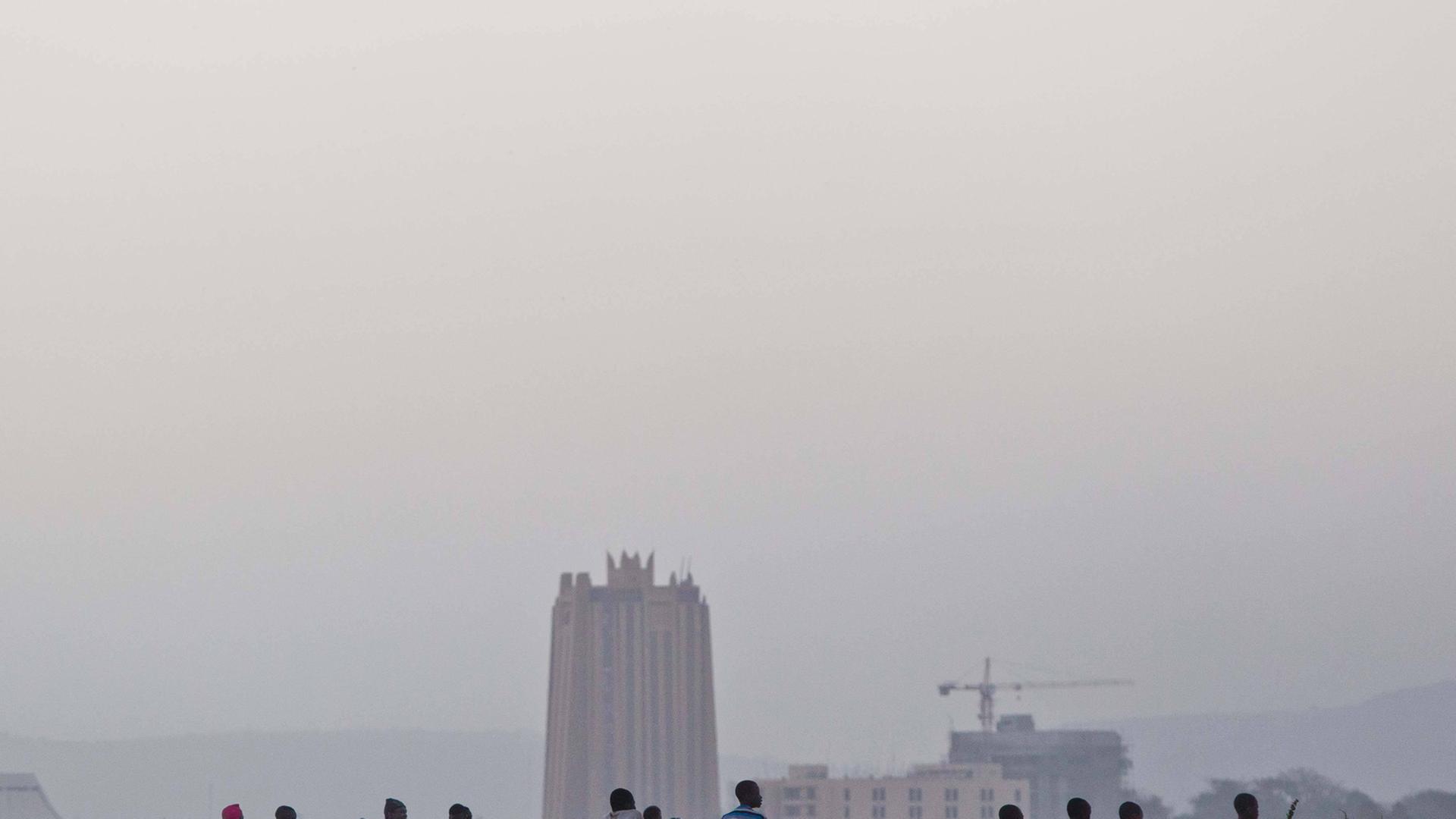 Menschen sitzen auf einer Mauer, im Hintergrund ein Hochhaus und mehrere kleinere Gebäude in Bamako. Menschen sitzen auf einer Mauer, im Hintergrund ein Hochhaus und mehrere kleinere Gebäude in Bamako.