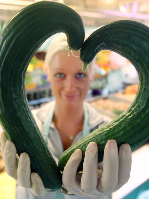 Eine Gemüsehändlerin zeigt am 30.06.2009 auf dem Isemarkt in Hamburg zwei krumme Gurken in Herzform.