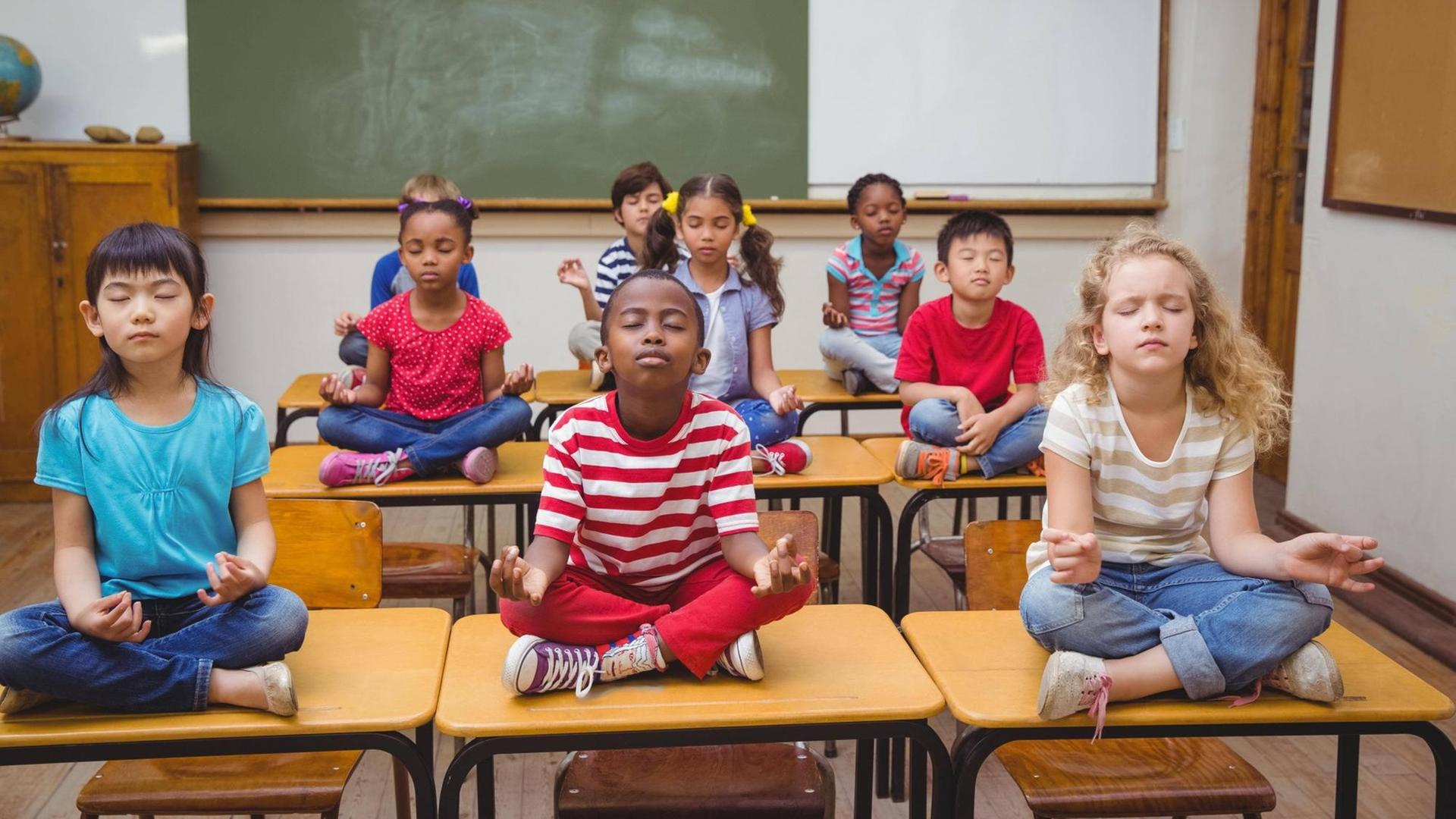 Grunschüler meditieren im Lotussitz auf den Schulbänken Grunschüler meditieren im Lotussitz auf den Schulbänken