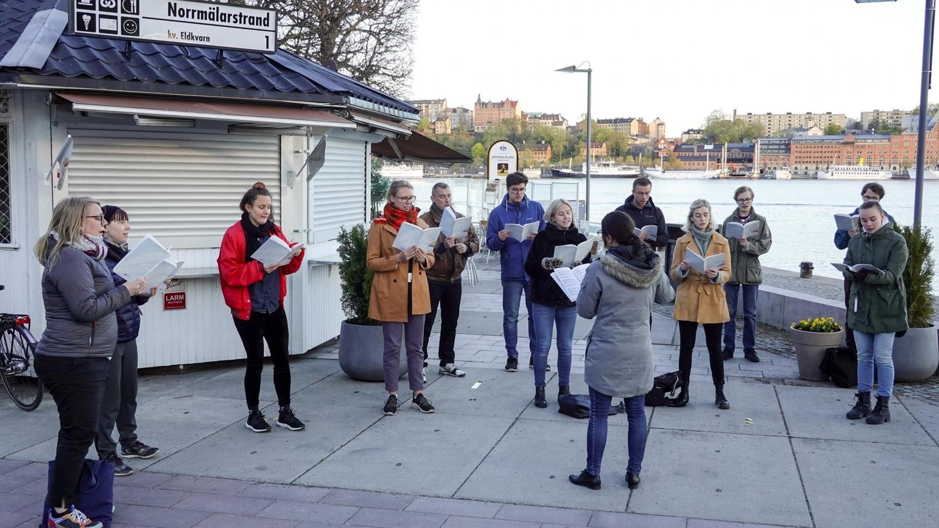 Eine Gruppe von Menschen steht in Abstand zueinander draußen im Freien und singt. Eine Gruppe von Menschen steht in Abstand zueinander draußen im Freien und singt.