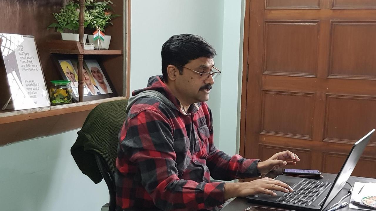 Ein Mann in kariertem Hemd mit Brille und Schnauzer sitzt in seinem Büro vor dem Laptop und tippt.
