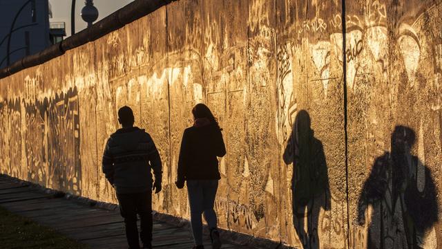 Eine Frau und ein Mann gehen am 18.04.2015 in Berlin im Licht der untergehenden Sonne an der East Side Gallery spazieren.