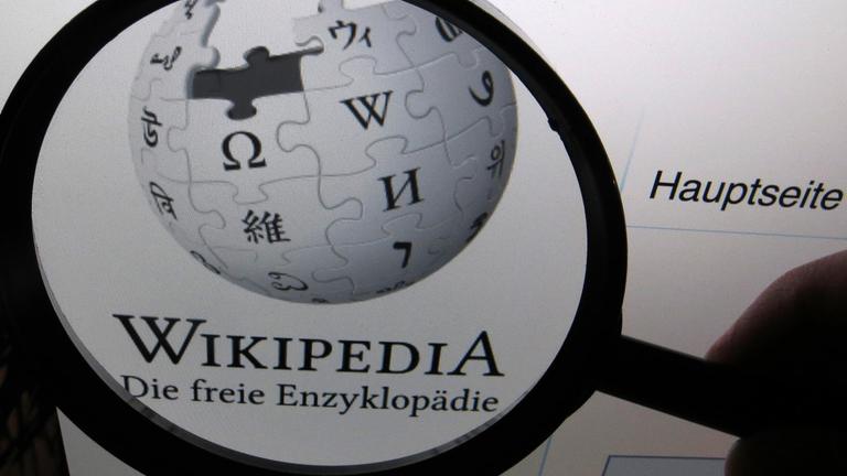 Auf einem Computerbildschirm ist das Logo der deutschen Version der freien Enzyklopädie Wikipedia durch eine Lupe vergrößert auf einem Computerbildschirm zu sehen. 