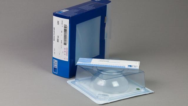 Ein Brustimplantat in Originalverpackung liegt auf einem Tisch, daneben eine blaue Umverpackung mit dem Logo von PIP.