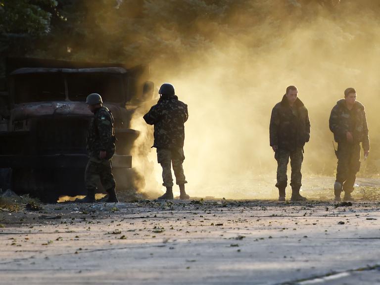 Ukrainische Soldaten stehen neben einem zerstörten Militärfahrzeug in der ostukrainischen Hafenstadt Mariupol.