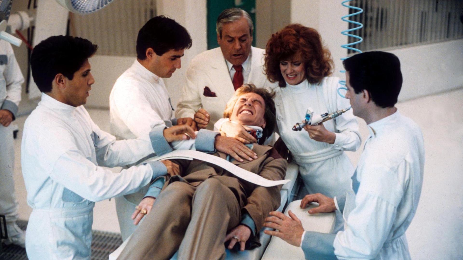 Martin Short liegt in der Filmszene festgezurrt auf einer Bare, umringt von 5 Ärzten mit einer riesigen Spritze. Martin Short liegt in der Filmszene festgezurrt auf einer Bare, umringt von 5 Ärzten mit einer riesigen Spritze.