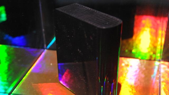 Das Bild zeigt eine schwarze Festplatte in einem gläsernem Schaukasten, in dem sich buntes Licht bricht.