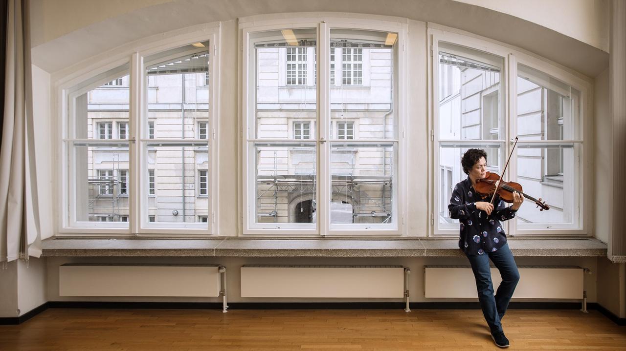 Die Bratscherin hat sich ihr Instrument spielend an das Fensterbrett eines halbrunden großen Fensters gelehnt. Die Bratscherin hat sich ihr Instrument spielend an das Fensterbrett eines halbrunden großen Fensters gelehnt.