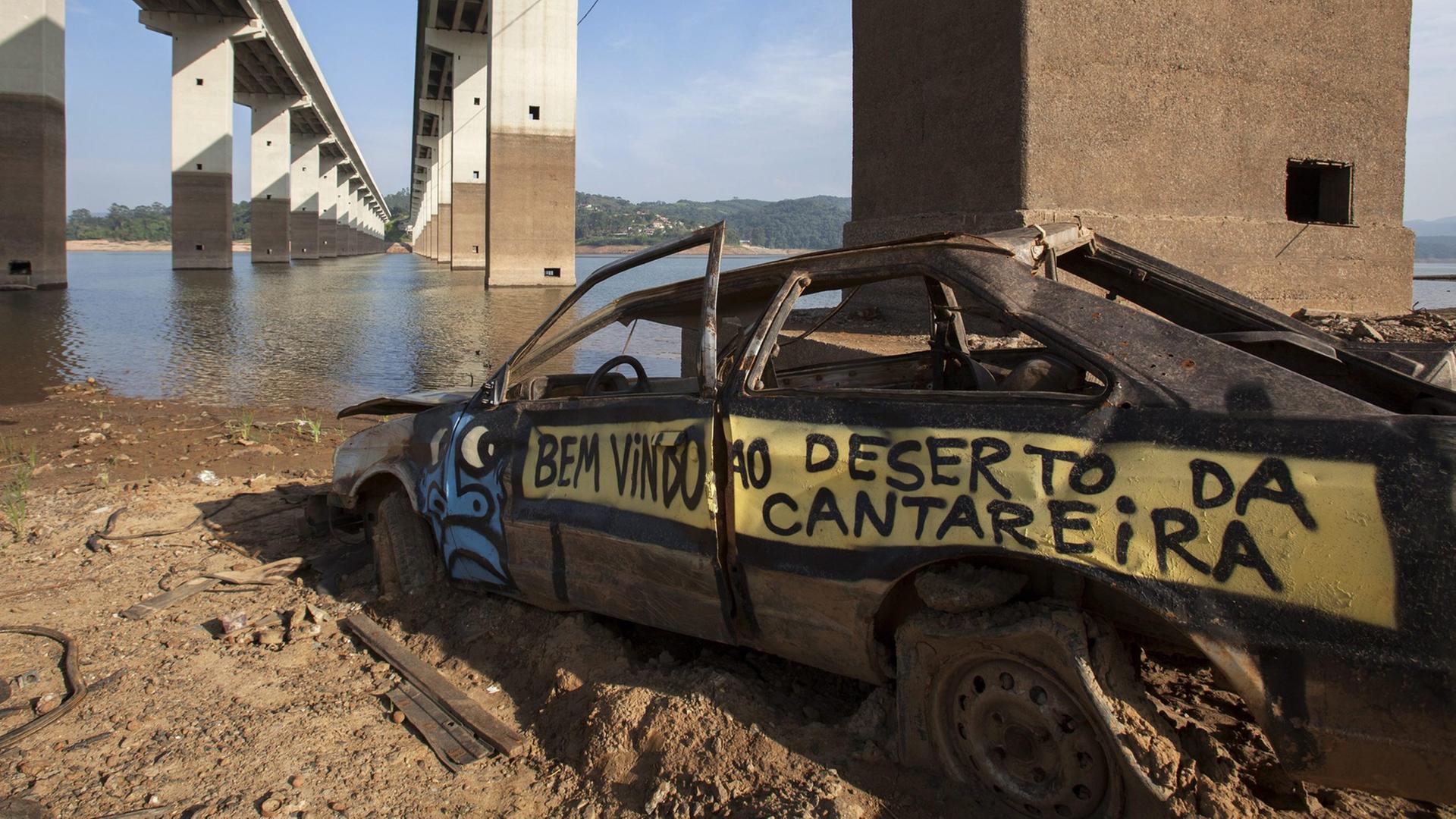 Brückenpfeiler und ein altes Autowrack sind an einem Fluss in Sao Paulo Brasilien zu sehen. Der Fluss führt ungewöhnlich wenig Wasser. Brückenpfeiler und ein altes Autowrack sind an einem Fluss in Sao Paulo Brasilien zu sehen. Der Fluss führt ungewöhnlich wenig Wasser.
