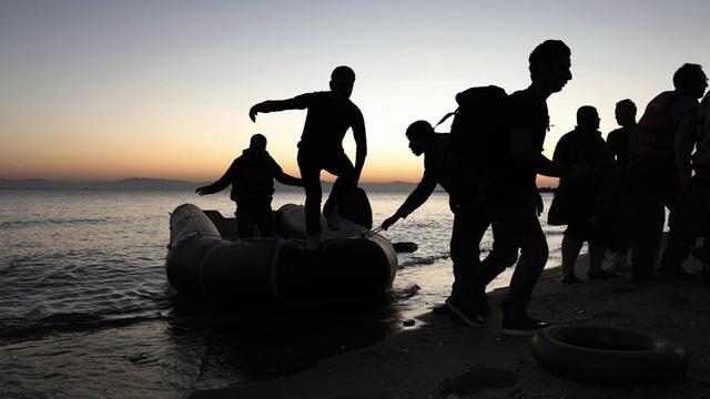 Flüchtlinge entsteigen einem Schlauchboot und gehen an Land.