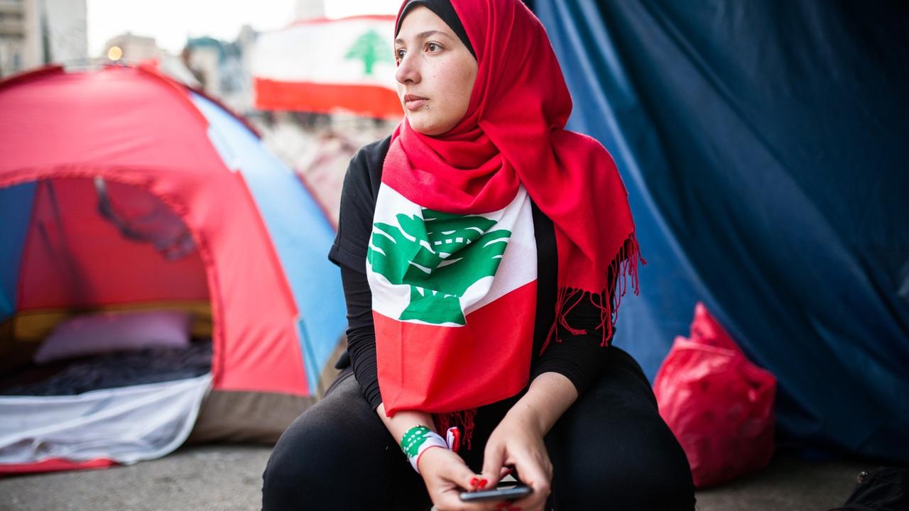 Eine Demonstrantin sitzt mit einer libanesischen Flagge vor Zelten
