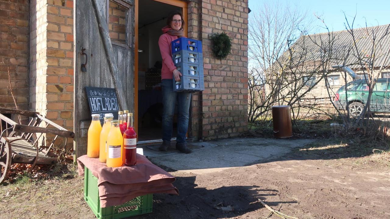Eine Frau steht mit Kästen in den Armen vor einem Hofladen. Eine Frau steht mit Kästen in den Armen vor einem Hofladen.