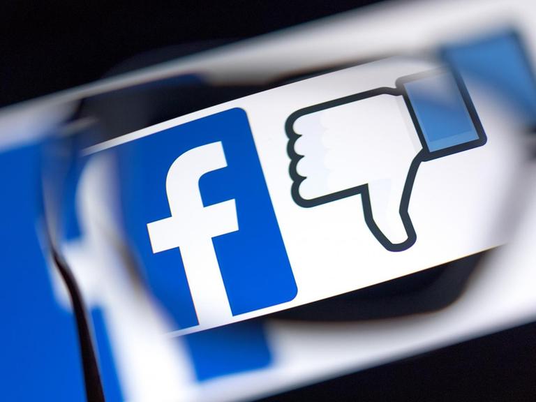 Das Logo des sozialen Netzwerks Facebook und das Zeichen für "Gefällt mir nicht" (Daumen runter) werden auf einem Bildschirm angezeigt.