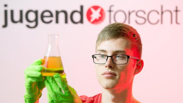 Felix Knothe aus Sachsen posiert in Künzelsau im Rahmen des Nachwuchswettbewerbs "Jugend forscht" vor dem Logo des Wettbewerbs.