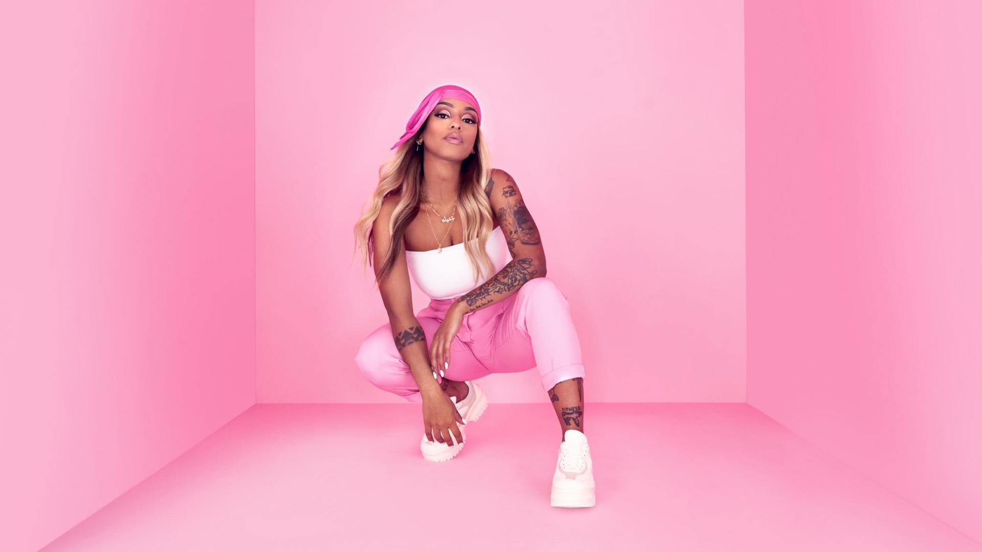 Die Rapperin Nura posiert in der Hocke vor einem pinken Hintergrund. Die Rapperin Nura posiert in der Hocke vor einem pinken Hintergrund.