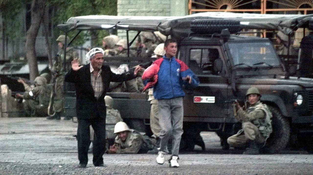 Zwei Usbeken mit erhobenen Händen, hinter ihnen Soldaten