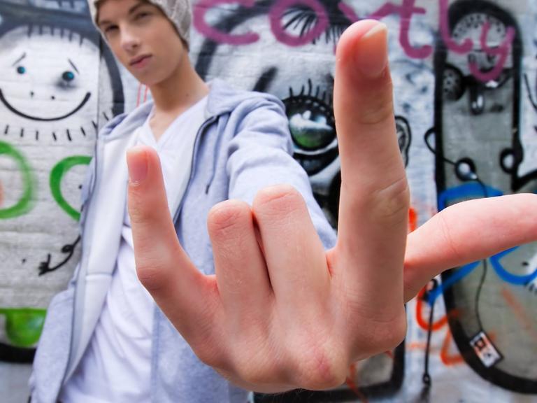 Ein cool blickender jugendlicher Mann gestikuliert vor einer Wand mit Graffiti