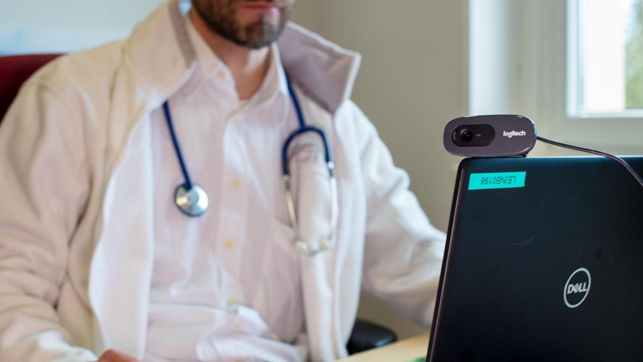 Hausarzt spricht während einer Videosprechstunde in seiner Praxis mit einer Patientin Hausarzt spricht während einer Videosprechstunde in seiner Praxis mit einer Patientin