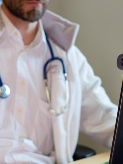 Hausarzt spricht während einer Videosprechstunde in seiner Praxis mit einer Patientin
