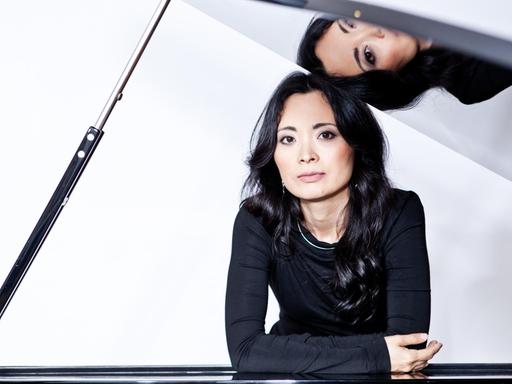 Ein Portrait der Pianistin Rei Nakamura am Flügel, deren Gesicht sich im Instrumentendeckel spiegelt