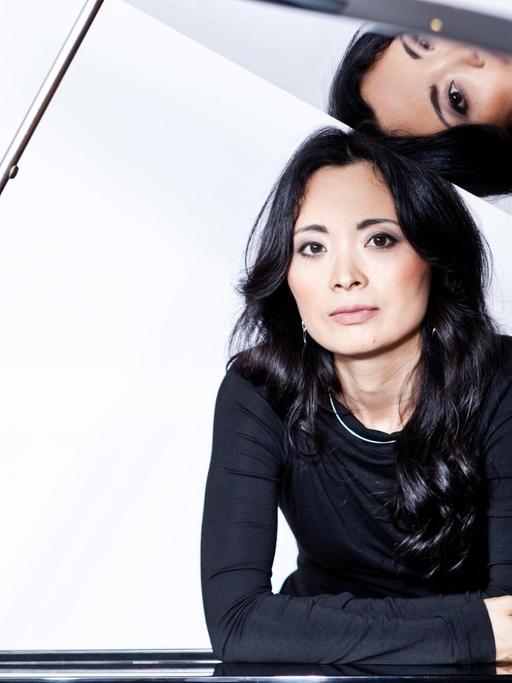 Ein Portrait der Pianistin Rei Nakamura am Flügel, deren Gesicht sich im Instrumentendeckel spiegelt