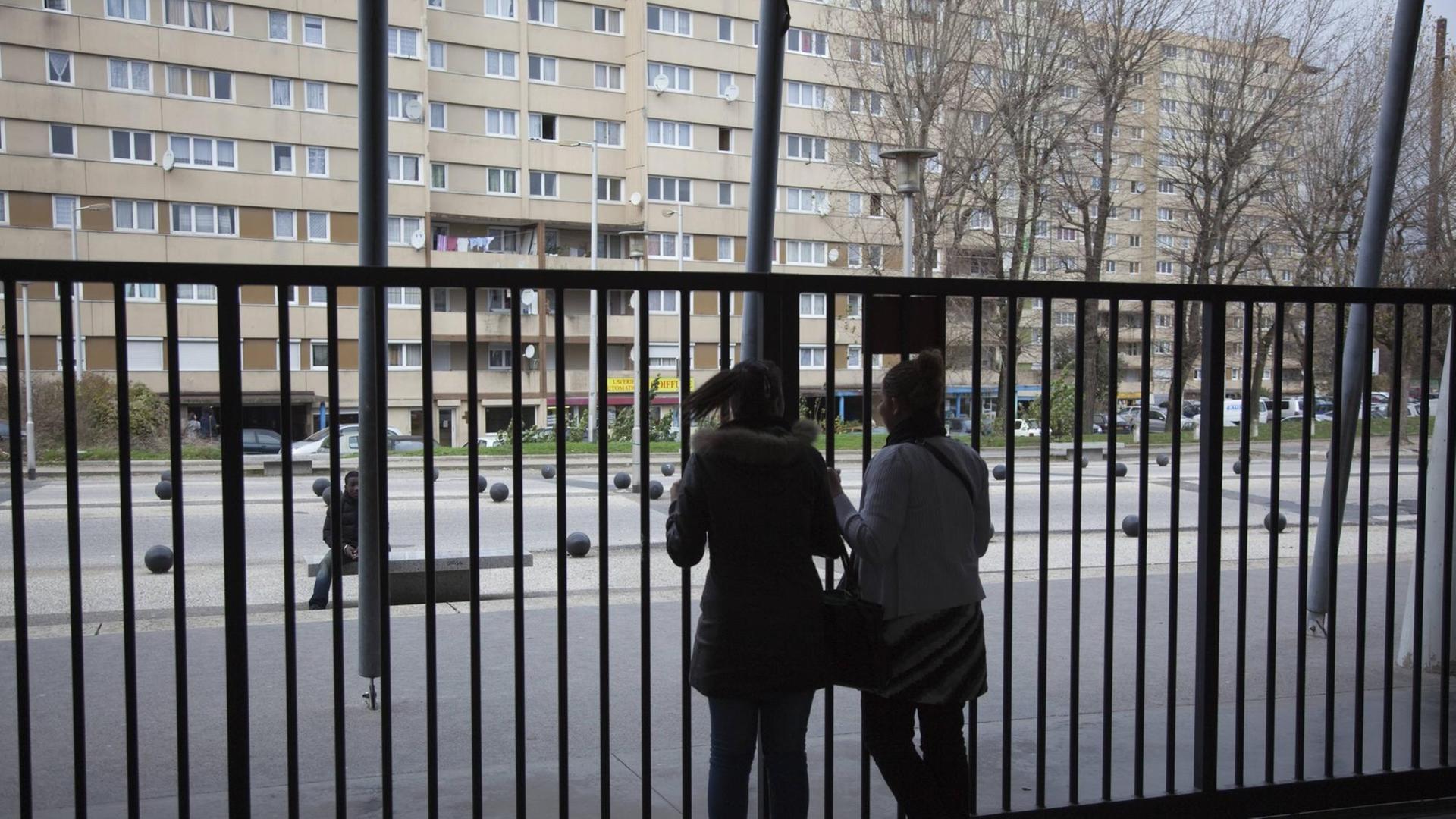 Zwei Schülerinnen am Alfred Nobel Gymnasium im Pariser Vorort Clichy Sous Bois. 2009. Zwei Silhouetten vor einem hohen Zaun, im Hintergrund ein runtergekommener Plattenbau. Zwei Schülerinnen am Alfred Nobel Gymnasium im Pariser Vorort Clichy Sous Bois. 2009. Zwei Silhouetten vor einem hohen Zaun, im Hintergrund ein runtergekommener Plattenbau.