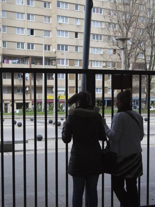 Zwei Schülerinnen am Alfred Nobel Gymnasium im Pariser Vorort Clichy Sous Bois. 2009. Zwei Silhouetten vor einem hohen Zaun, im Hintergrund ein runtergekommener Plattenbau.