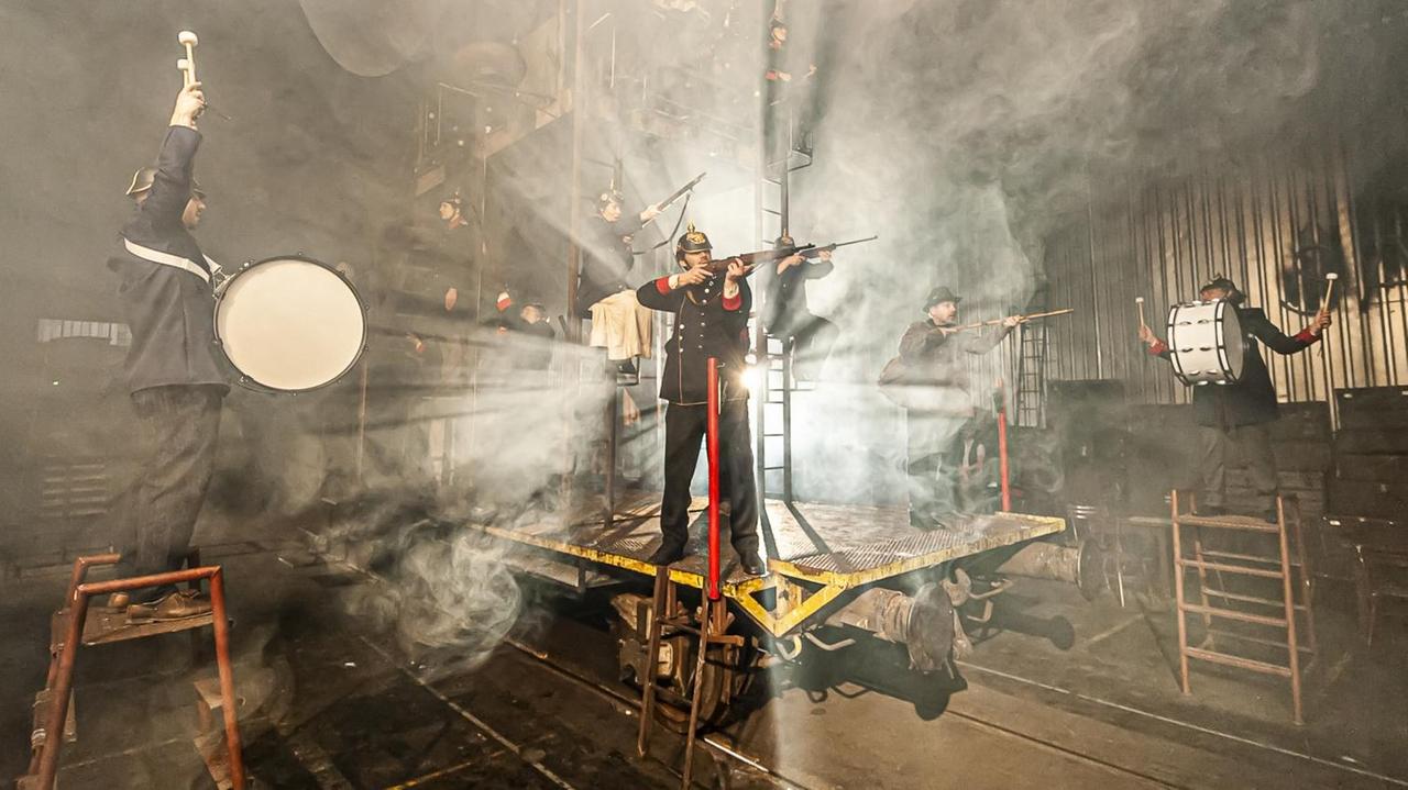 Von hinten stark überleuchtet haben Uniformierte des frühen 20. Jahrhunderts einen bizarr anmutenden Bühnenauftritt. Von hinten stark überleuchtet haben Uniformierte des frühen 20. Jahrhunderts einen bizarr anmutenden Bühnenauftritt.