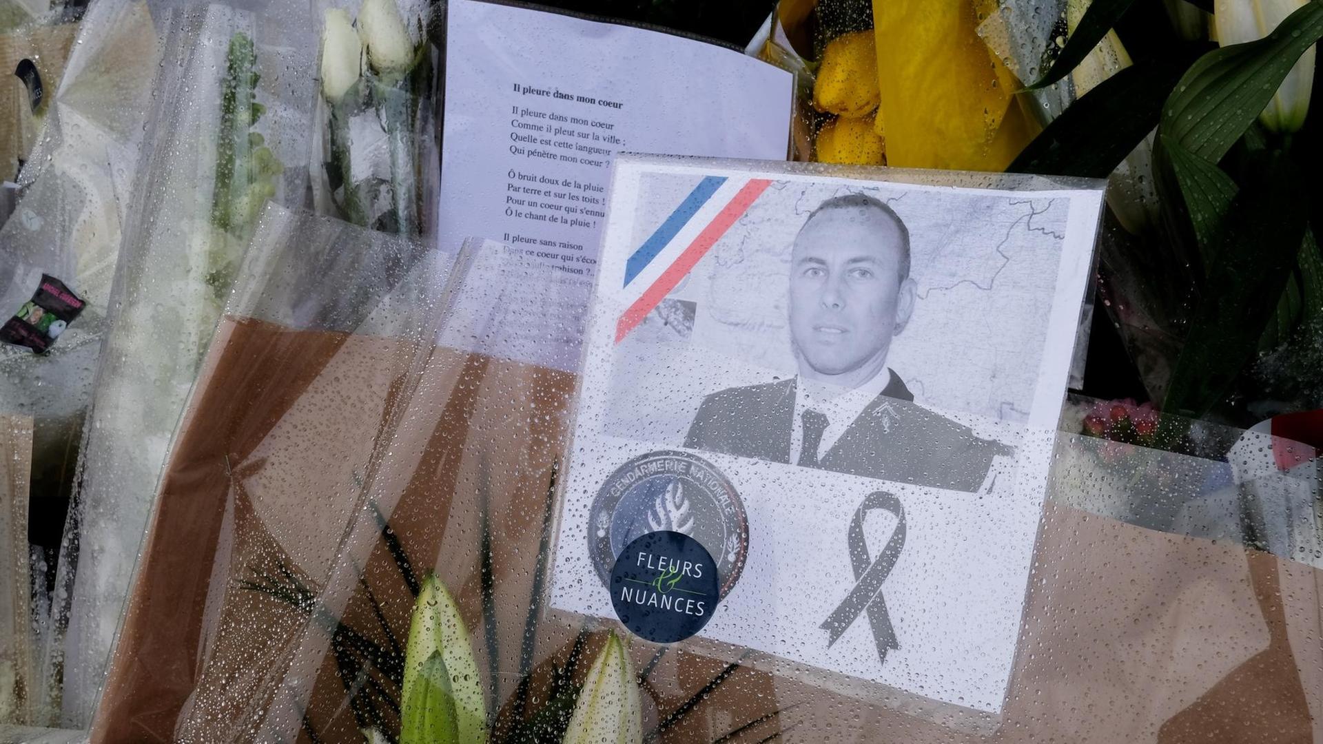Blumen mit dem Portrait des bei einer Geiselnahme in Trébes getöteten Polizeibeamten Arnaud Beltrame liegen vor dessen Arbeitsplatz, der Gendarmerie in Carcassonne im Südwesten Frankreichs.